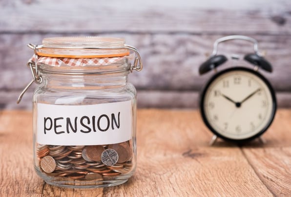 A jar of pension savings on a wooden table with a ticking alarm clock behind it now able to added to more as the annual allowance for UK pensions has increased.