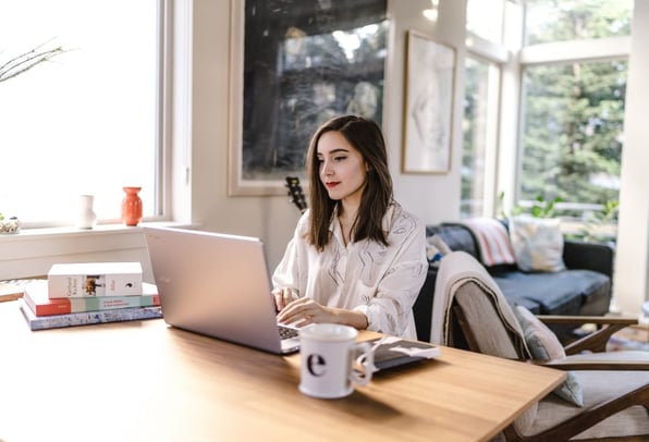 A woman working on her laptop at her dining room table with a large mug of coffee ready to claim her working from home tax relief.