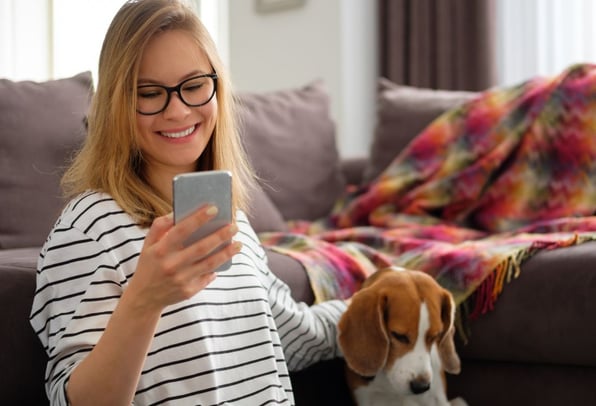 A young woman and her beagle sitting on the sofa as she looks at her finances happily on her phone. 