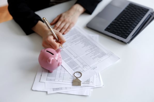 Person looking at finances with a laptop, notebook and piggybank
