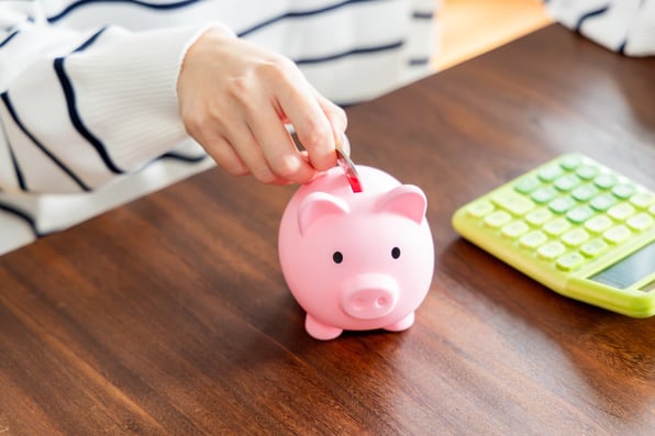 Woman’s hands putting a coin into a piggybank, with a calculator next to her