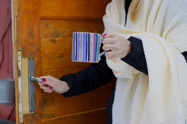 Woman standing at an open door with a cup of tea