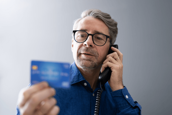 A man reading out his card details over the phone being scammed by a cybercriminal