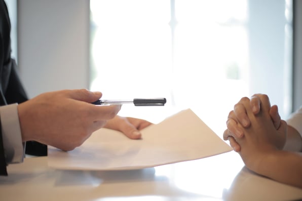 A person is handing over paper and pen to someone else deciding between a mortgage broker or a bank. 